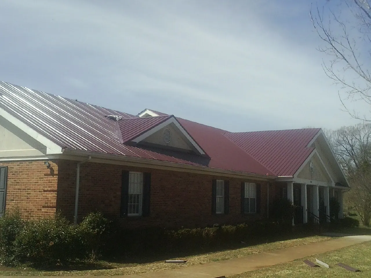 Red metal roof with gabled entries on a long brick building, from a Hail Damage Roof Repair job in Ukiah