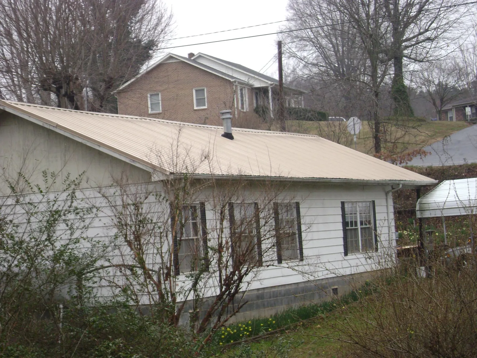 Tan metal roof on a white sided house set into a hillside — Commercial Roofing by Roofing Brothers in Ukiah